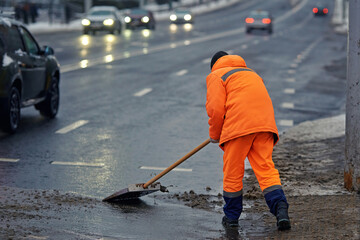 Utility worker throwing wet snow from sidewalk on road. Worker with shovel throw snow and slush, clearing footpath. Worker cleaning snowy pedestrian crossing, shovels melting snow onto the road - Powered by Adobe