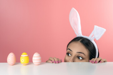 Beautiful young woman with pink bunny ears and Easter eggs on pink background. Minimal Easter concept.
