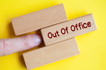 Finger pushing out wooden block with out of office text on yellow cover background