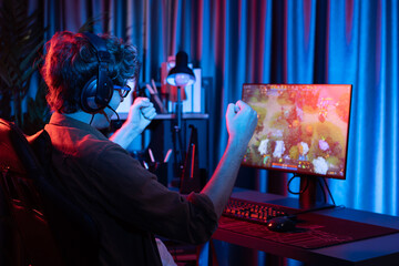 Host channel of young gaming streamer getting to win fighting Moba at battle arena with multiplays team, wearing headphone on pc monitor with back side image at neon digital light modern room. Gusher.