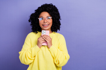Photo of dreamy woman dressed yellow sweater in eyewear hold smartphone look at eshop empty space isolated on violet color background