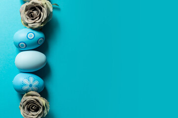 Gray flowers and decorated Easter eggs on blue background, top view.
