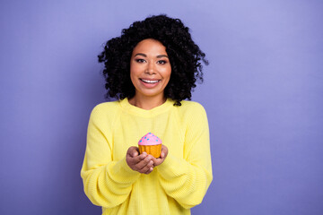 Photo of good mood kind woman with afro hairdo dressed yellow sweater hold tasty cupcake in arms...