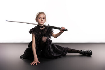 Halloween concept. Cute little witch in long black dress with sword. Isolated on white studio background with black floor.