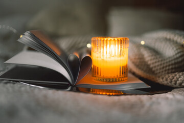 Scented candle with an open book with folded sheets in heart shape in bed with a warm blanket....