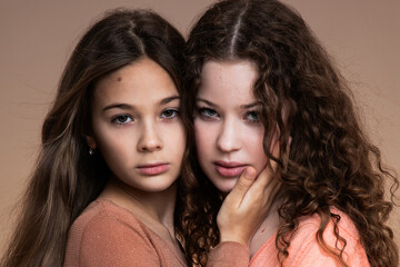 Studio portrait of two beautiful sisters in peach and beige shirts against beige background