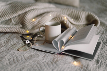 Cup of tea with an open book in bed with a warm blanket. Winter holiday season or Valentines Day....