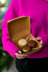 Female hands hold three macaroons on sticks in black, white and gold colors in a gift box