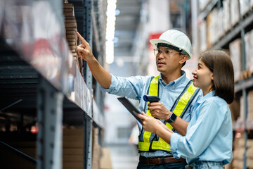 Warehouse staff working together using digital tablets to check the stock inventory on shelves in...