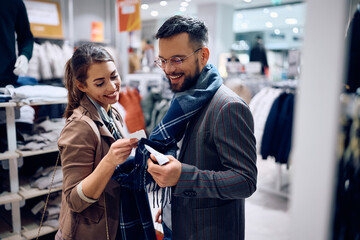 Happy couple looking at price tag while shipping at clothing store.