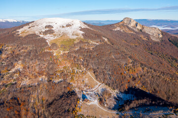 Beautiful autumn colorful view of a mountain lodge surrounded by a forest with dried leaves and the peak above the lodge covered with the first winter snow - aerial drone photo