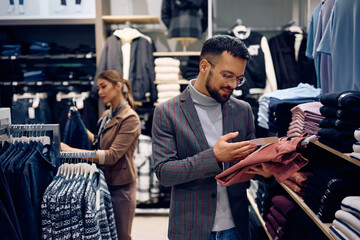 Happy man looking at price tag while shopping at clothing store.