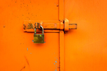 Padlock on orange color wooden gate forming a textured background.