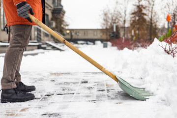 Close-up of a man cleaning and clearing snow in front of the house on a sunny and frosty day. Cleaning the street from snow on a winter day. Snowfall, and a severe snowstorm in winter.