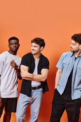 handsome multiracial male models in stylish urban clothes posing on orange backdrop, fashion