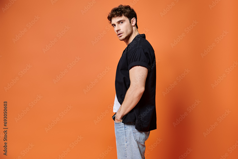 Wall mural appealing stylish man in casual outfit on orange backdrop looking at camera, fashion concept