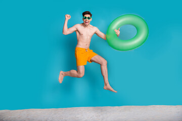 Full length photo of nice young male jump run raise fist inflatable ring dressed stylish yellow...