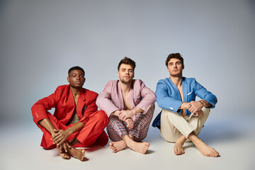 Fototapeta premium appealing diverse men in vibrant trendy suits sitting on floor with crossed legs, fashion concept