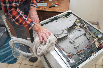 man is a jack of all trades, he removed the lid of the washing machine and wipes the dust inside...