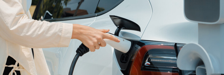 Young woman put EV charger to recharge electric car's battery from charging station. Alternative...