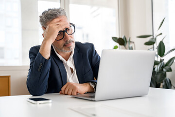 Thoughtful male office employee using laptop indoors, looking at laptop screen with puzzled face expression, businessman solving tasks, having problems with finance - obrazy, fototapety, plakaty