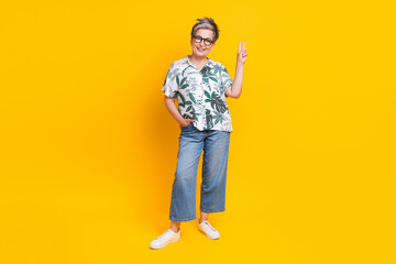 Full length photo of lovely grandma posing showing v-sign symbol wear trendy tropical print garment isolated on yellow color background
