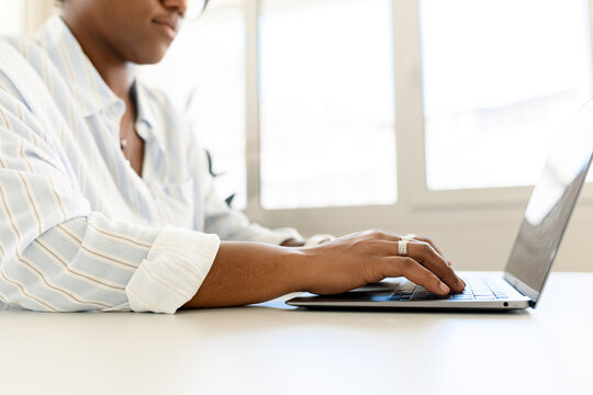 Cropped picture of african-american woman using laptop, female employee is typing on the keyboard, answering emails, multiracial female freelancer in casual wear working remotely from co-working
