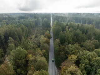 Aerial view of a driving green car through a misty forest