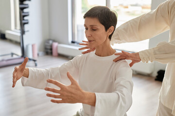 Waist up shot of brunette senior woman doing qigong concentration exercise and holding hands in air...