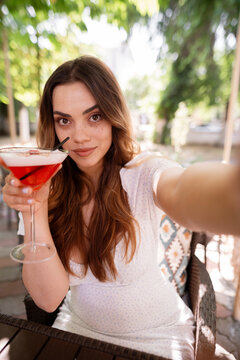 Woman taking a selfie with cocktail for social media content creation on a holiday vacation in a restaurant. Happy women taking pictures with drinks