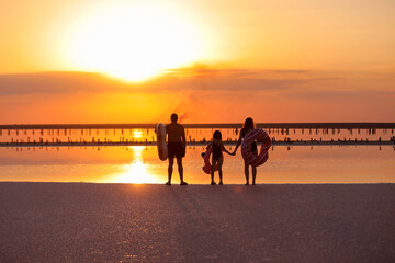 happy family walk on sunset by the sea. mom, dad and child daughter having fun on summer holiday...