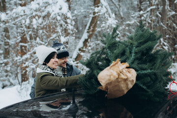 Christmas mood. A couple in love decorates a Christmas tree on the roof of their car with garlands.
