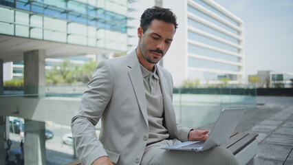 Focused businessman texting laptop urban bench closeup. Latin man sipping coffee
