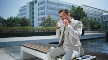 Relaxed businessman eating sandwich at wooden bench. Italian man lunch break