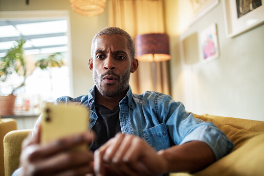 Man sitting on couch looking surprised at phone