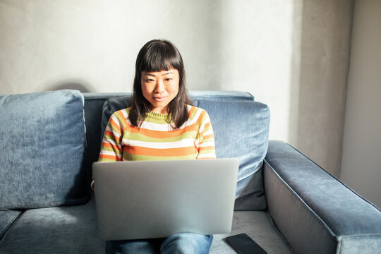 Smiling woman on sofa using typing laptop at home