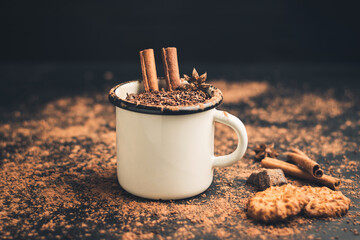 Homemade spicy hot chocolate drink with cinnamon stick, star anise, grated chocolate in enamel mug on dark background with cookies, cacao powder and chocolate pieces - obrazy, fototapety, plakaty