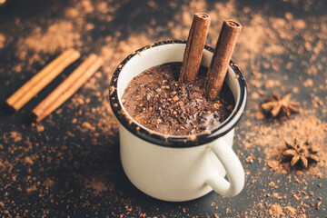 Homemade spicy hot chocolate drink with cinnamon stick, star anise, grated chocolate in enamel mug...