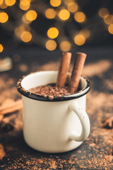 Homemade spicy hot chocolate drink with cinnamon stick, grated chocolate in enamel mug on dark...