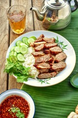 Thai food fried pork with rice and cucumber coriander,banana leaf background,antique style teapot and tea glass, thai called moo tod