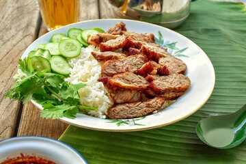 Thai food fried pork with rice and cucumber coriander,banana leaf background,antique style teapot and tea glass, thai called moo tod