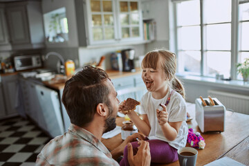 Father and daughter enjoying breakfast with chocolate spread in sunny kitchen