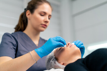 portrait of a beautician doctor cleaning a client's skin with a cotton sponge before starting a...
