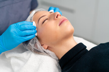 close-up, a cosmetologist cleans a client's skin with a cotton swab before starting a beauty and health procedure