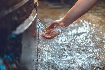 Beautiful photo of a hand under a stream of clear spring water. The woman lowered her hand to touch...