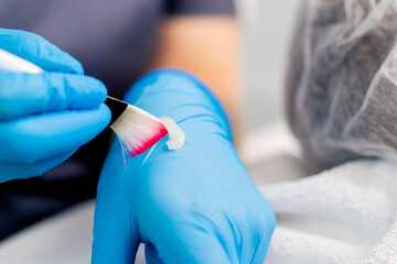 Close-up of a beautician doctor's hand in gloves holding a brush and applying a mask to check the consistency in a beauty salon