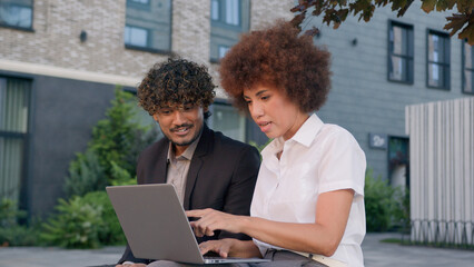 Two diverse business partners coworkers multiracial workers with laptop in city discuss online data...