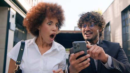 Multiracial business colleagues coworkers friends African businesswoman Arabian Indian businessman walking in city with mobile phone win success high five gesture achieve online good result happy