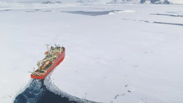 Icebreaker breaks through pack ice on its way. Red Nuclear icebreaker clears its pass in Antarctica. Vessel navigating: Aerial view. Featuring Research Boat slicing through Southern Ocean's ice.