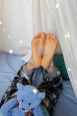 the bare foot of a child lying in a wigwam tent, soft toy bear sitting on a child's bottom. Good...